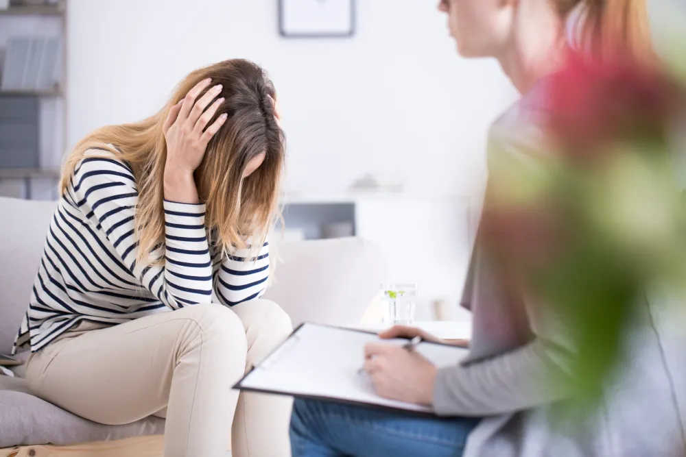 Trauma therapy in anaheim with women sitting with hands on head with therapist.