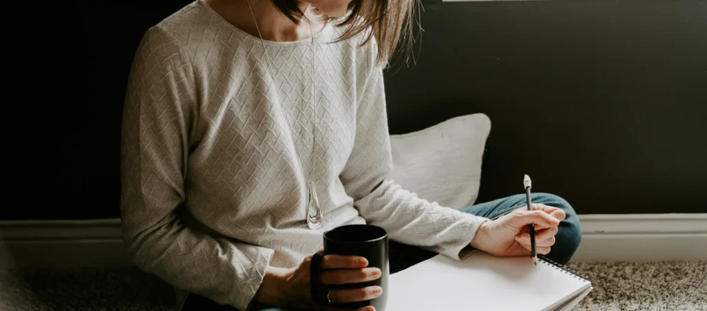 Woman holding a mug and writing in a notebook, accompanying a guide to hangxiety meaning